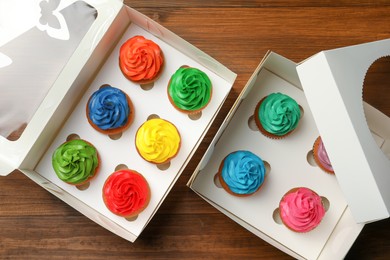 Boxes with delicious colorful cupcakes on wooden table, flat lay