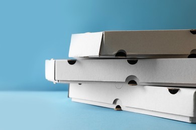 Stack of empty pizza boxes on light blue background, closeup. Space for text