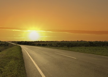 Image of Empty asphalt road through field at sunset