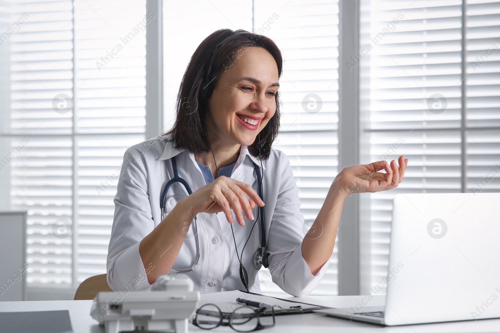 Photo of Doctor with headset and laptop consulting patient online in office. Hotline service