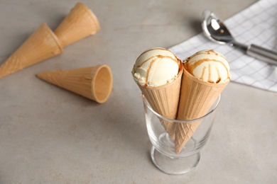 Photo of Delicious ice cream in waffle cones with caramel sauce served on table