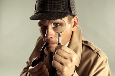 Photo of Male detective with smoking pipe looking through magnifying glass on grey background
