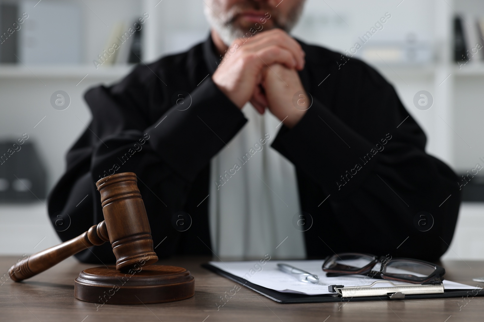 Photo of Judge with gavel and papers sitting at wooden table indoors, closeup