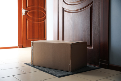 Photo of Cardboard box on rug near door. Parcel delivery service