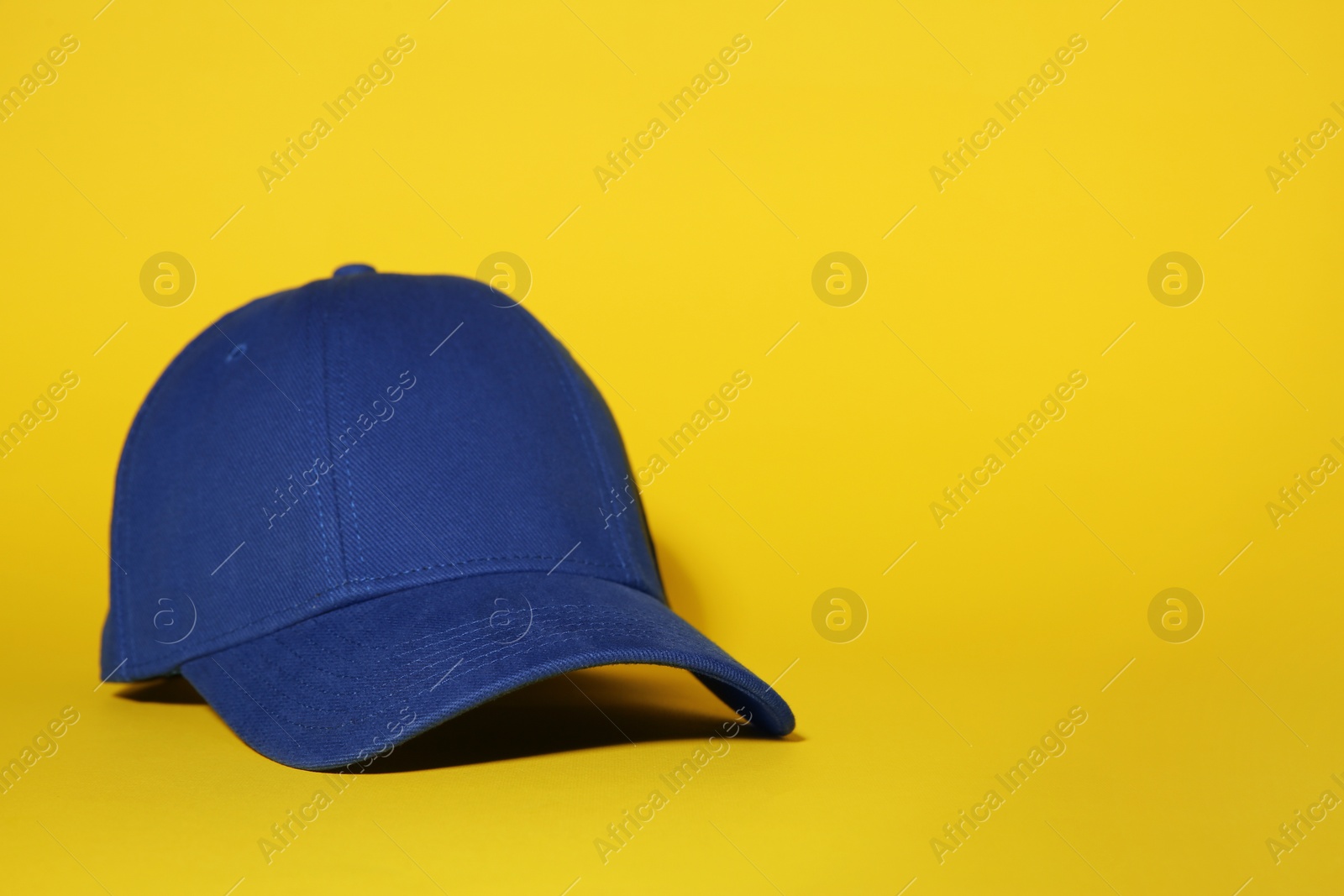 Photo of Stylish blue baseball cap on yellow background, space for text