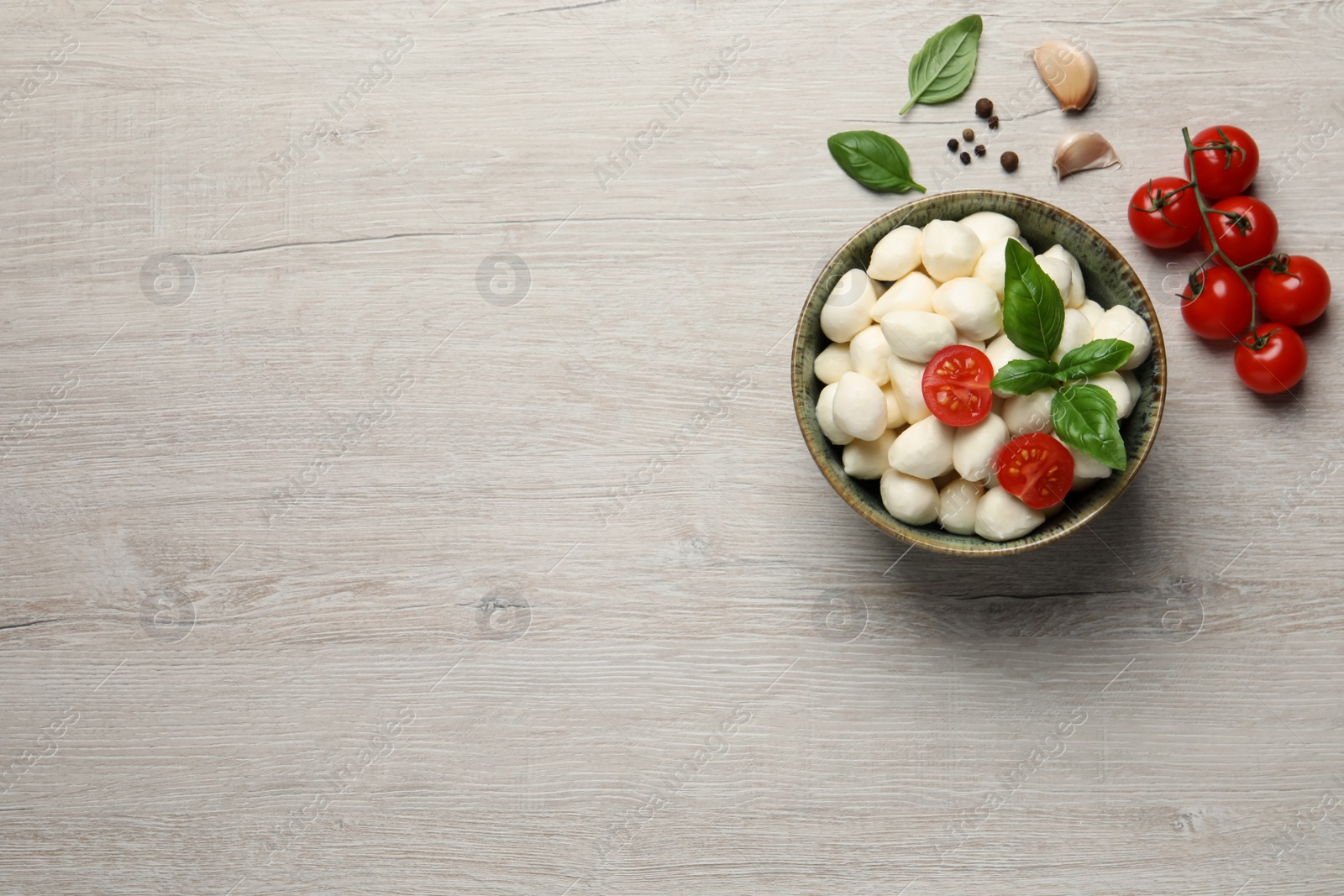Photo of Delicious mozzarella balls in bowl, tomatoes and garlic on white wooden table, flat lay. Space for text