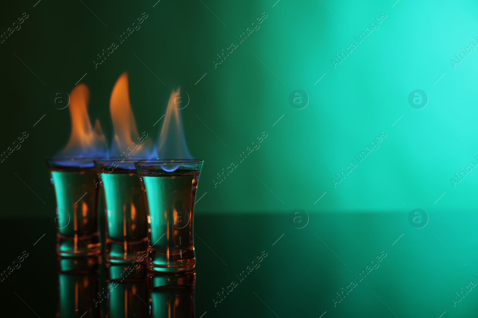 Photo of Flaming vodka in shot glasses on green background, space for text