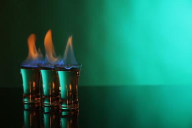 Photo of Flaming vodka in shot glasses on green background, space for text