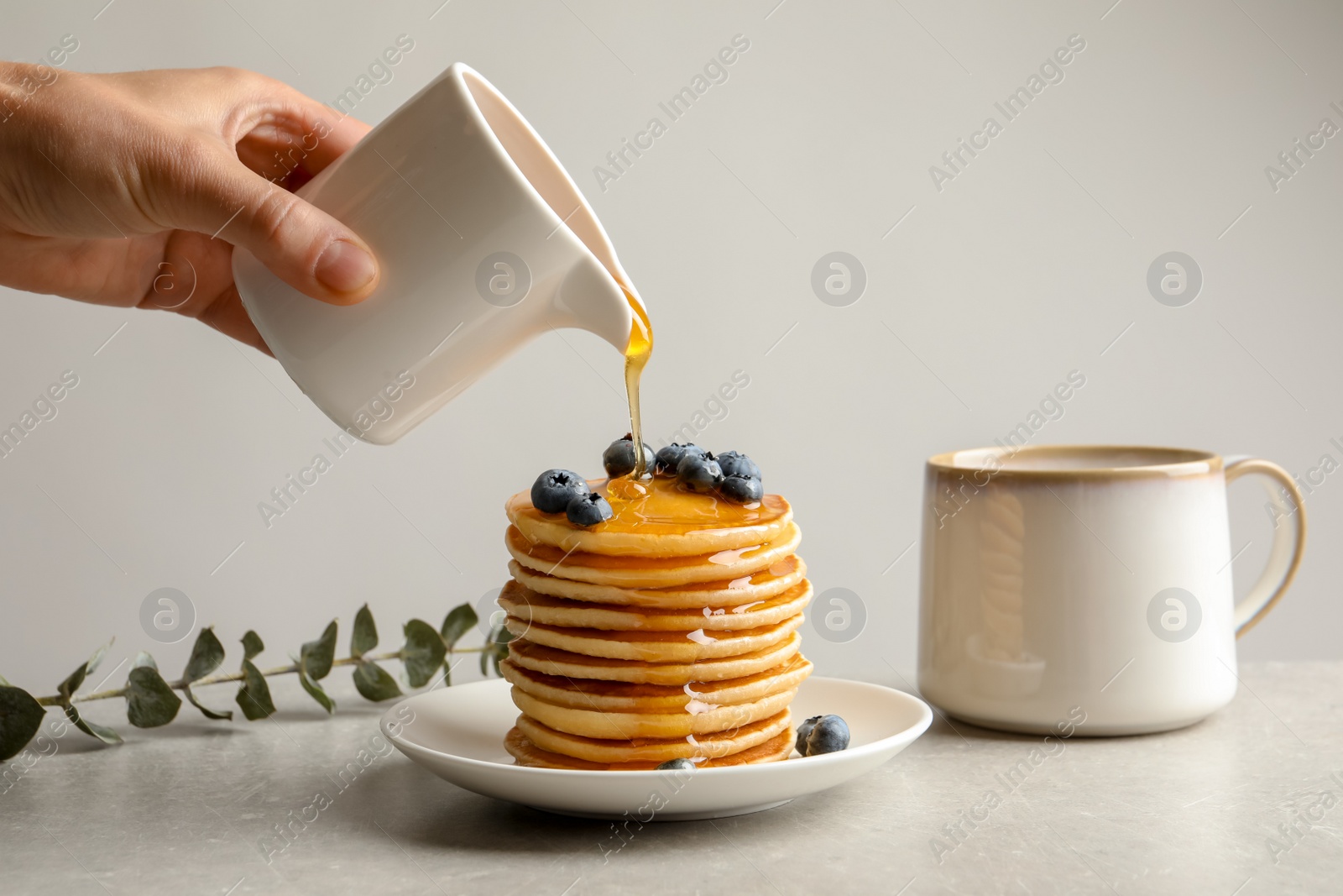 Photo of Woman pouring honey onto tasty pancakes with berries on table, closeup