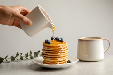 Woman pouring honey onto tasty pancakes with berries on table, closeup