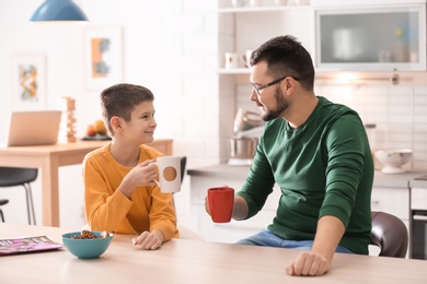 Little boy and his dad drinking tea together in kitchen