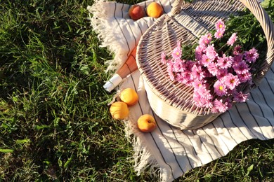 Photo of Picnic basket, flowers, peaches and bottle of wine on blanket outdoors