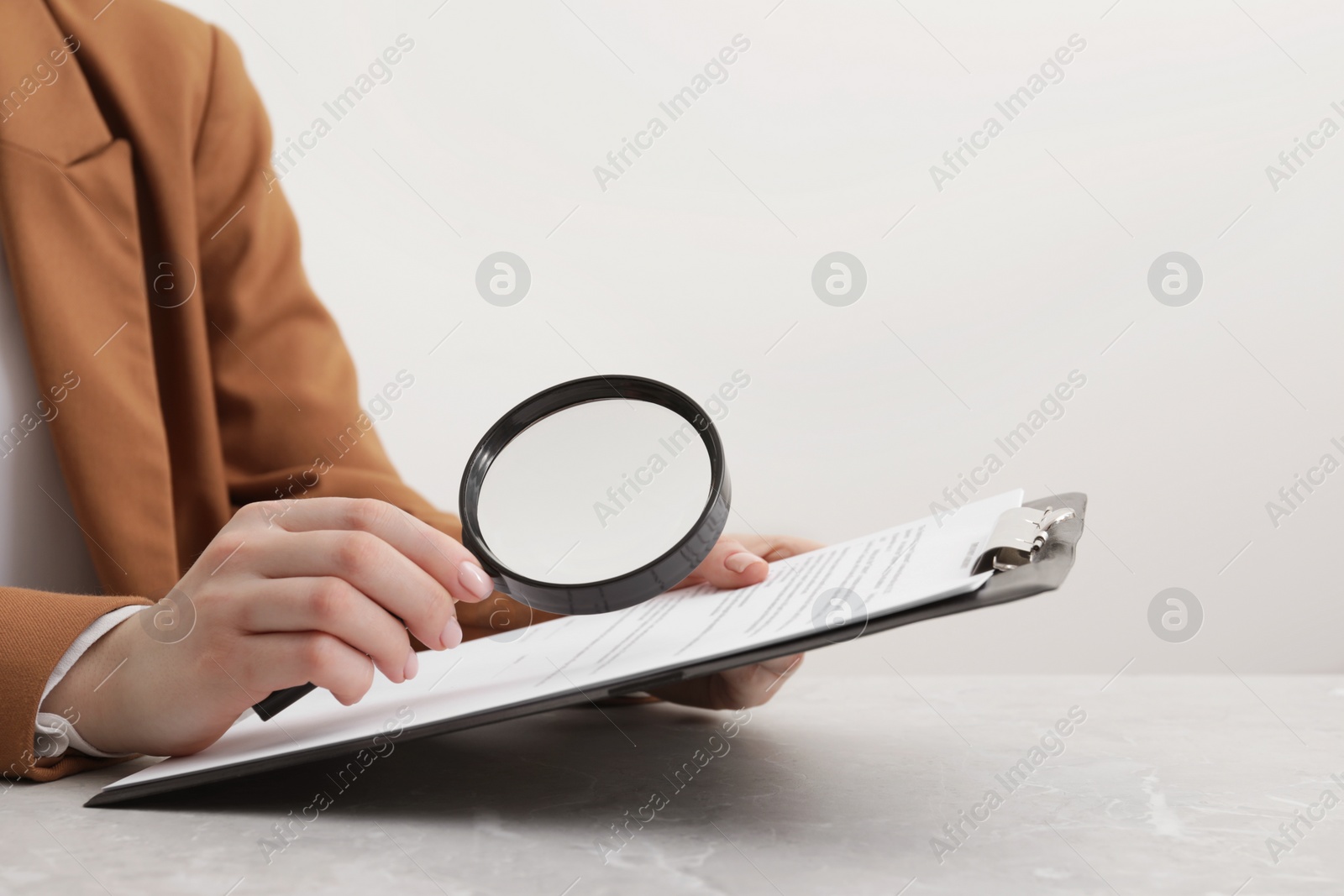 Photo of Woman looking at document through magnifier at light gray table, closeup. Searching concept