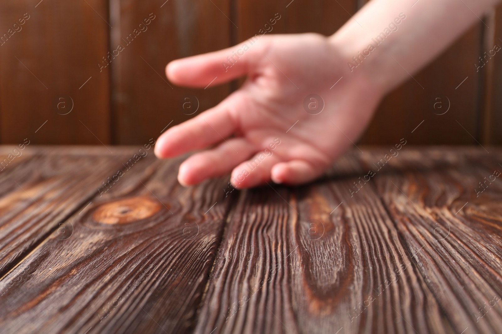 Photo of Woman holding hand above wooden table, selective focus. Space for text