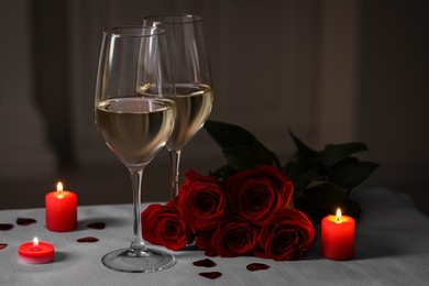 Photo of Glasses of white wine, rose flowers and burning candles on grey table against blurred background. Romantic atmosphere