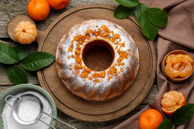 Homemade yogurt cake with tangerines, powdered sugar and green leaves on wooden table, flat lay