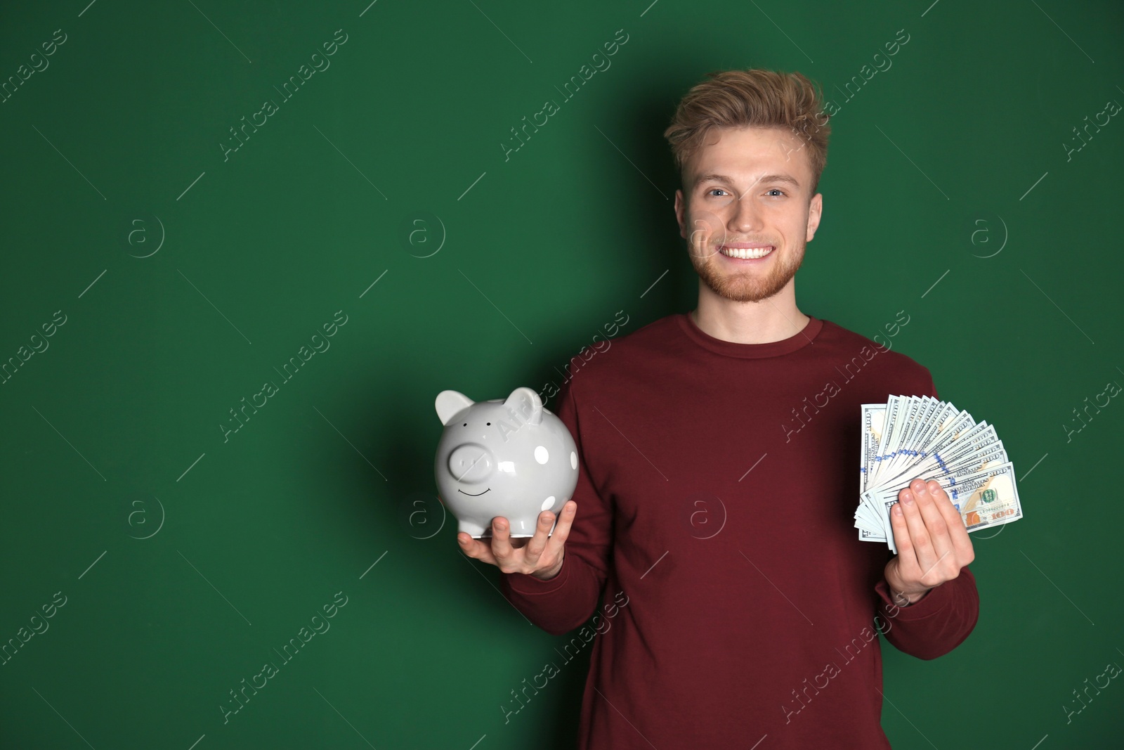 Photo of Young man with piggy bank and money on color background. Space for text