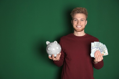 Young man with piggy bank and money on color background. Space for text