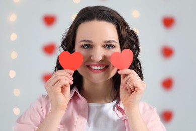 Photo of Beautiful young woman with red paper hearts indoors, view from camera. Valentine's day celebration in long distance relationship