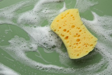 Yellow sponge with foam on green background, top view