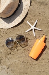 Photo of Blank bottle of sunscreen, starfish and beach accessories on sand, flat lay