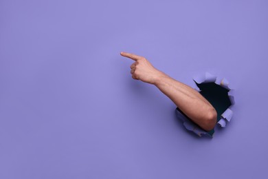 Photo of Special promotion. Man pointing at something through hole in purple paper, closeup. Space for text