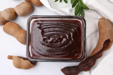 Photo of Bowl of tasty tamarind sauce and fresh pods on light table, flat lay