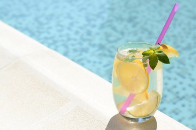 Photo of Refreshing water with lemon slices and mint near swimming pool. Space for text