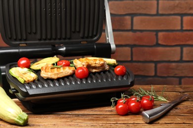 Photo of Electric grill with tasty meat, rosemary and vegetables on wooden table