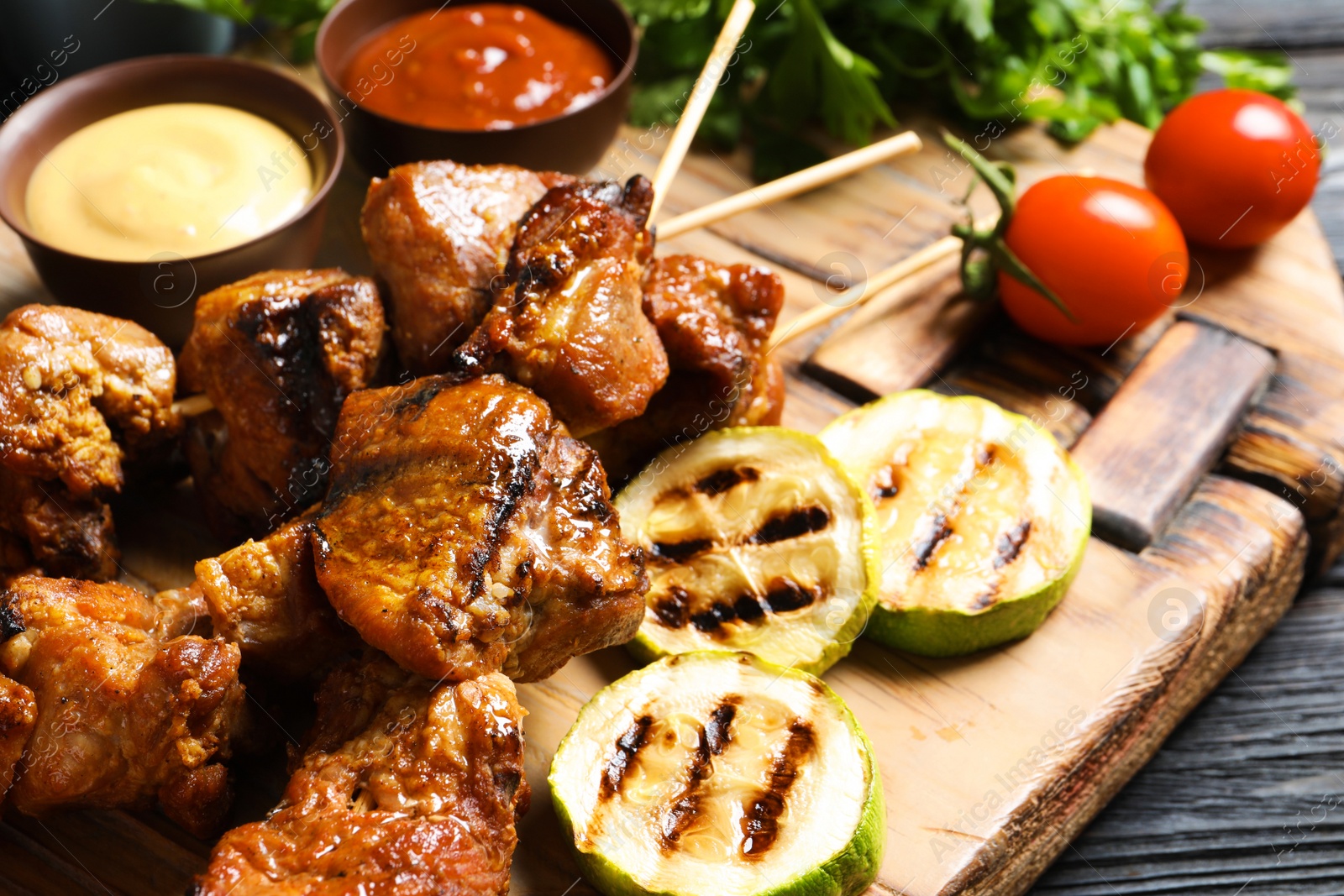 Photo of Delicious barbecued meat served with garnish and sauces on wooden board, closeup