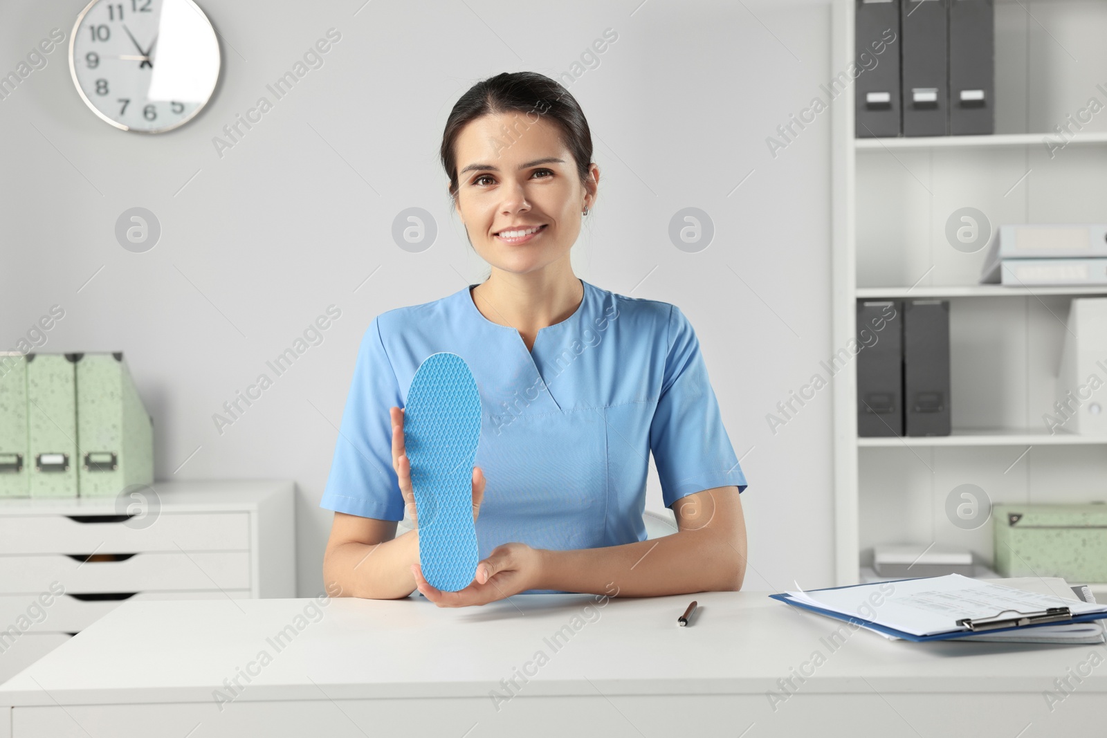 Photo of Beautiful female orthopedist showing insole at table in hospital