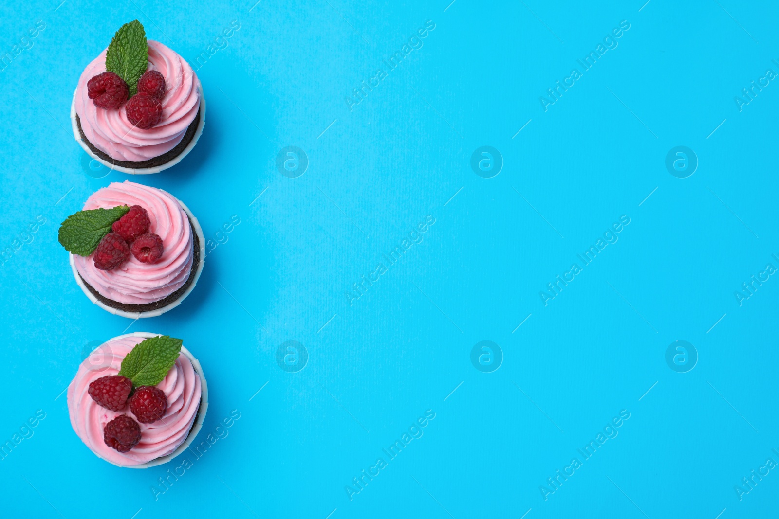 Photo of Delicious cupcakes with cream and raspberries on light blue background, flat lay. Space for text