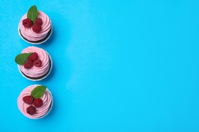 Delicious cupcakes with cream and raspberries on light blue background, flat lay. Space for text