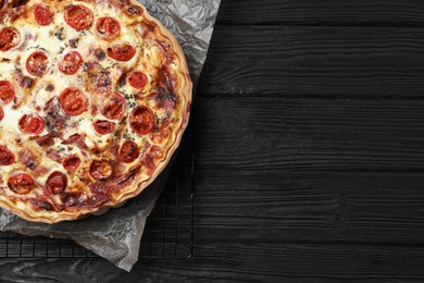 Photo of Delicious homemade quiche with prosciutto and tomatoes on black wooden table, top view. Space for text