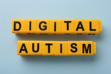 Phrase Digital Autism made of yellow cubes on light blue background, flat lay. Addictive behavior