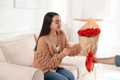 Photo of Happy woman receiving red tulip bouquet from man at home. 8th of March celebration