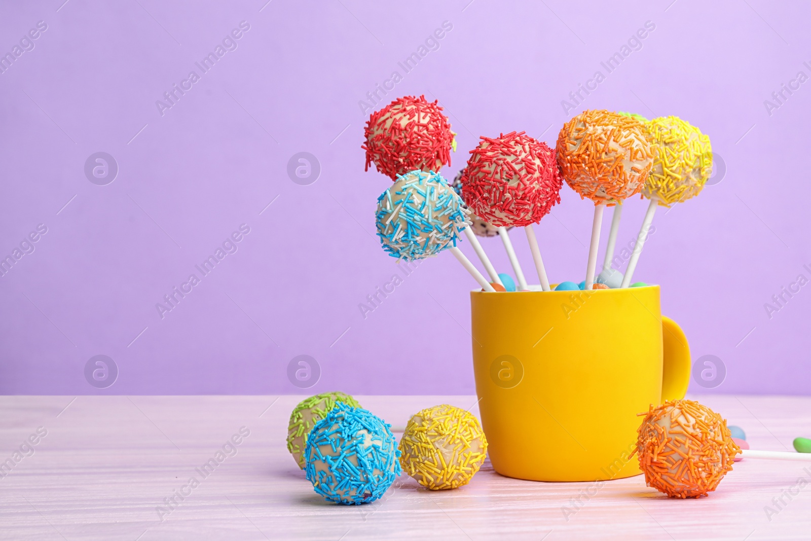 Photo of Cup with tasty cake pops on table against lilac background, space for text