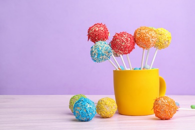 Photo of Cup with tasty cake pops on table against lilac background, space for text