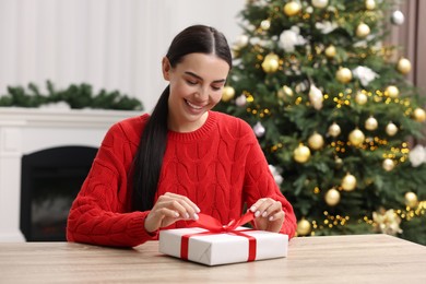 Photo of Happy woman opening Christmas gift at wooden table in room