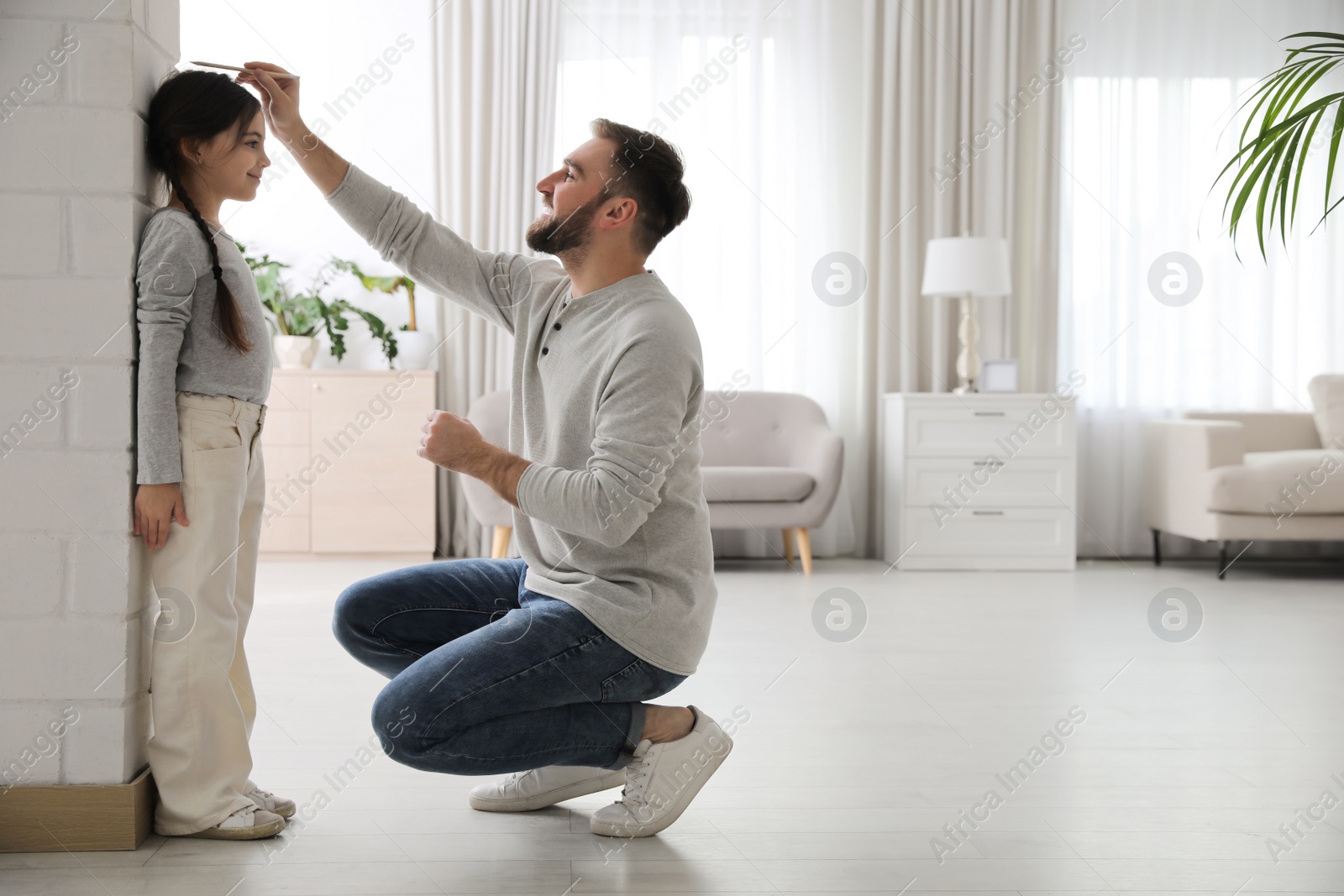 Photo of Father measuring daughter's height near white brick pillar at home, space for text