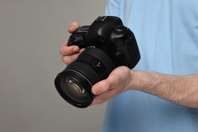 Photographer holding camera on grey background, closeup. Space for text