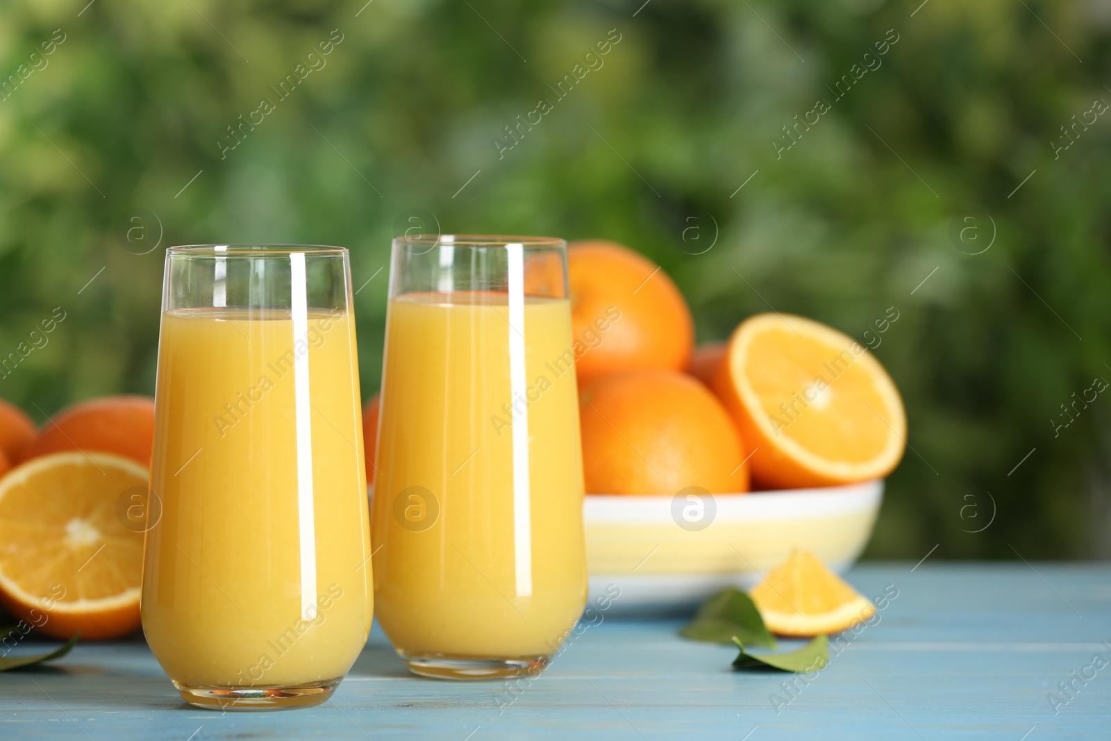 Photo of Delicious orange juice on light blue wooden table against blurred background. Space for text