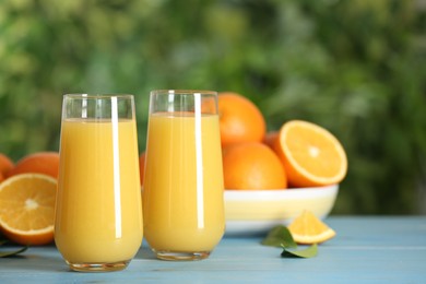 Photo of Delicious orange juice on light blue wooden table against blurred background. Space for text