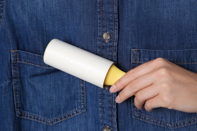 Photo of Woman cleaning denim shirt with lint roller, closeup