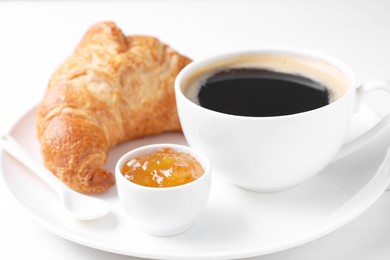 Photo of Fresh croissant, jam and coffee on white table, closeup. Tasty breakfast