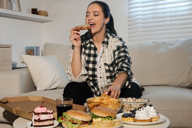 Photo of Happy overweight woman eating pizza and chips on sofa at home