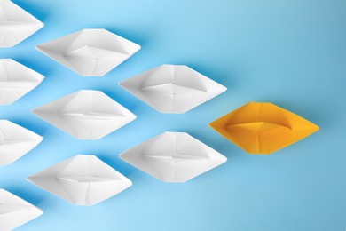 Photo of Group of paper boats following yellow one on light blue background, flat lay. Leadership concept