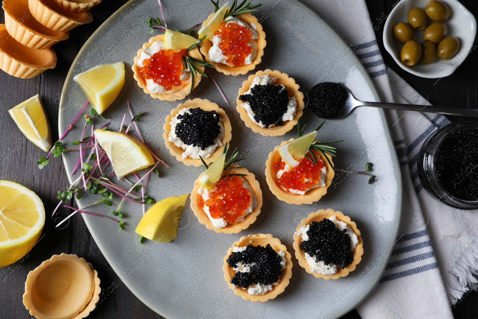 Photo of Delicious tartlets with red and black caviar served on wooden table, flat lay