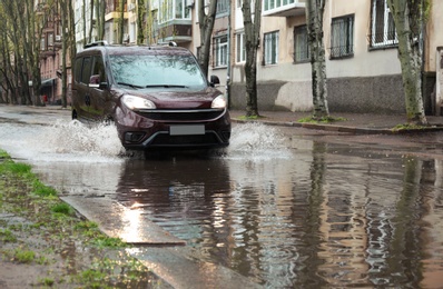 Photo of Car driving through large puddle outdoors on rainy day