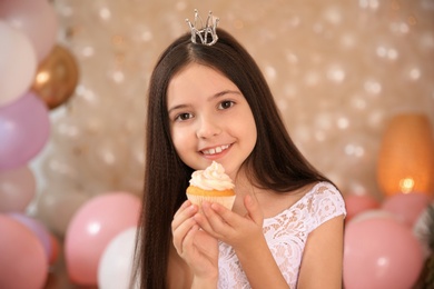 Photo of Happy little girl with birthday cupcake in beautifully decorated room at home